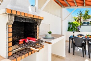 An outdoor grill with red sausages cooking, a table with chairs, and a potted plant. - Villa Dela - Two Bedroom Villa, Sleeps 4 (Vale Rebelho)