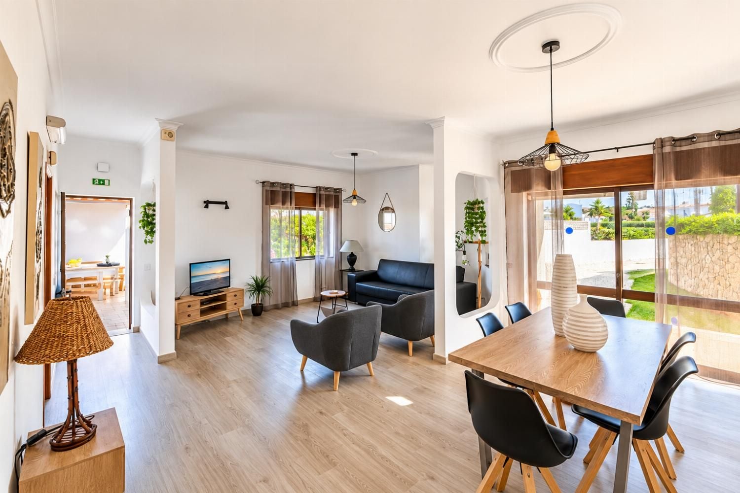 A modern living room with a sofa, dining table, and chairs, a television, and a lamp.
