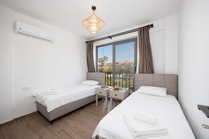 A hotel room with two single beds, a desk with a chair, a large window with curtains, an air conditioning unit, and a hanging light fixture. - Villa Lidya - Five Bedroom Villa, Sleeps 10 (Dalyan)