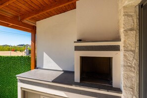 Zona cuina exterior amb una llar de pedra, sostre de fusta i vista a un paisatge verd.