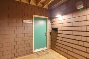 Um quarto com porta verde, placa de boas-vindas, prateleira pequena e parede revestida de azulejos.