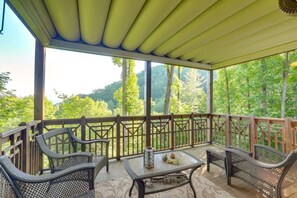 A covered outdoor seating area with wicker furniture and a table, overlooking a forested landscape. - Mtn-View Condo w Private Balcony in Burnsville (Burnsville)