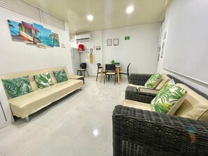 A hotel lobby with a sofa, chairs, a table, and a wall-mounted air conditioning unit. - Apartamentos Aury (San Andrés)