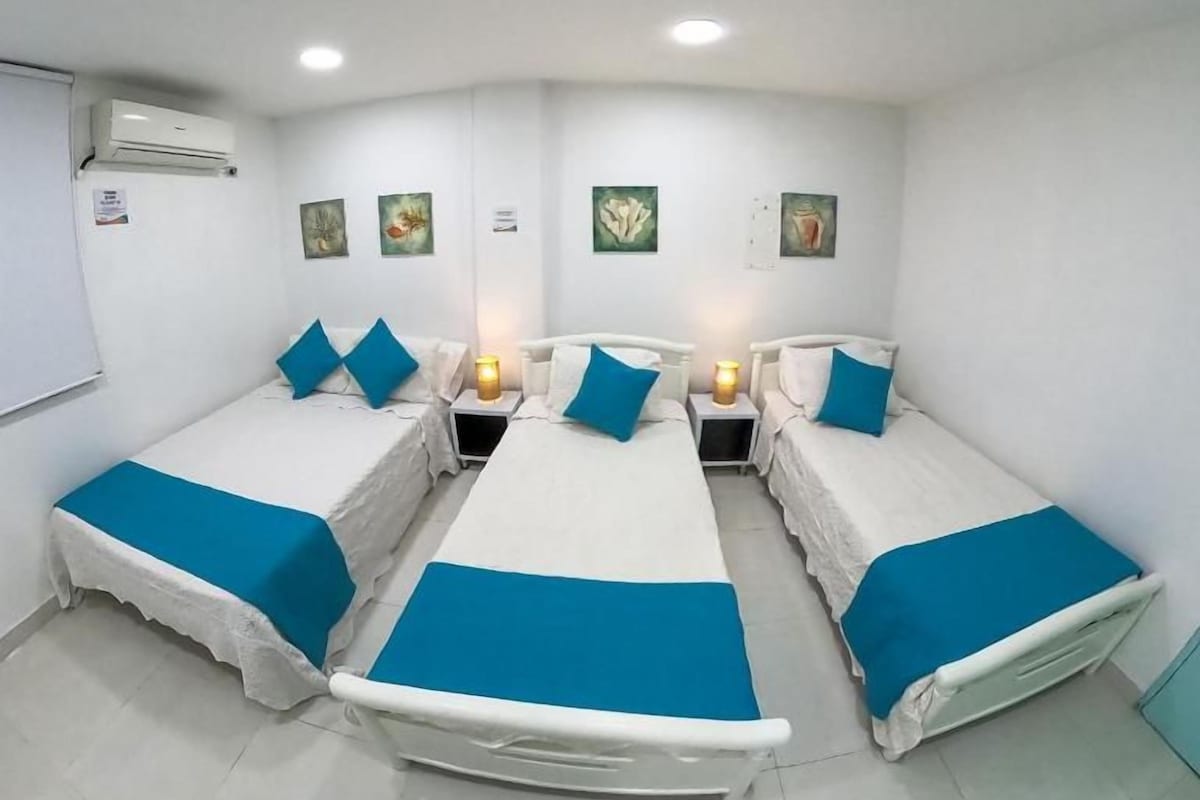 A hotel room with four single beds, white walls, and a white air conditioning unit.