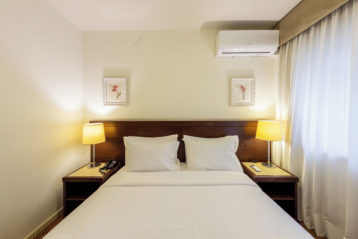 Ein Hotelzimmer mit einem großen Bett, zwei Nachttischen mit Lampen, einem Telefon und einer Klimaanlage.