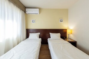 Ett hotellrum med två separata sängar, en sänggavel, ett nattduksbord med en lampa och en luftkonditioneringsanläggning.