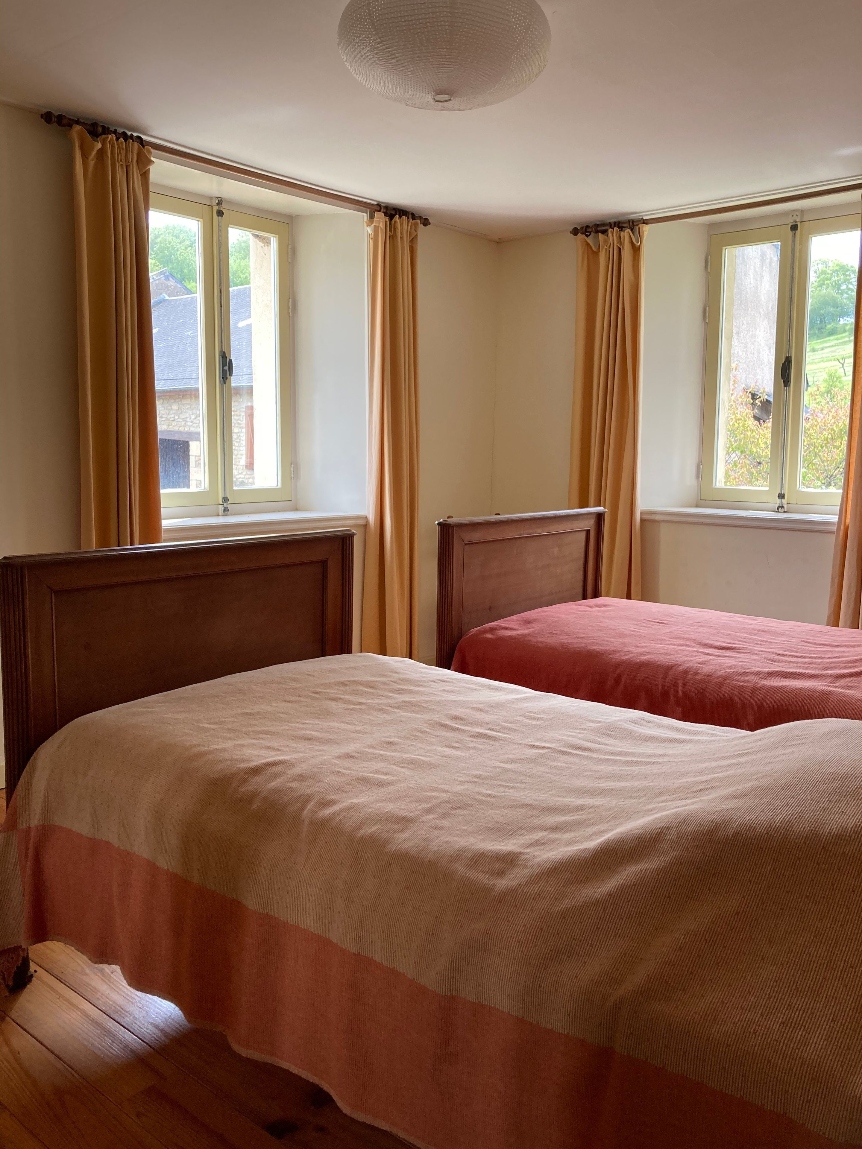 Una habitación con dos camas, suelo de madera y ventanas con cortinas.