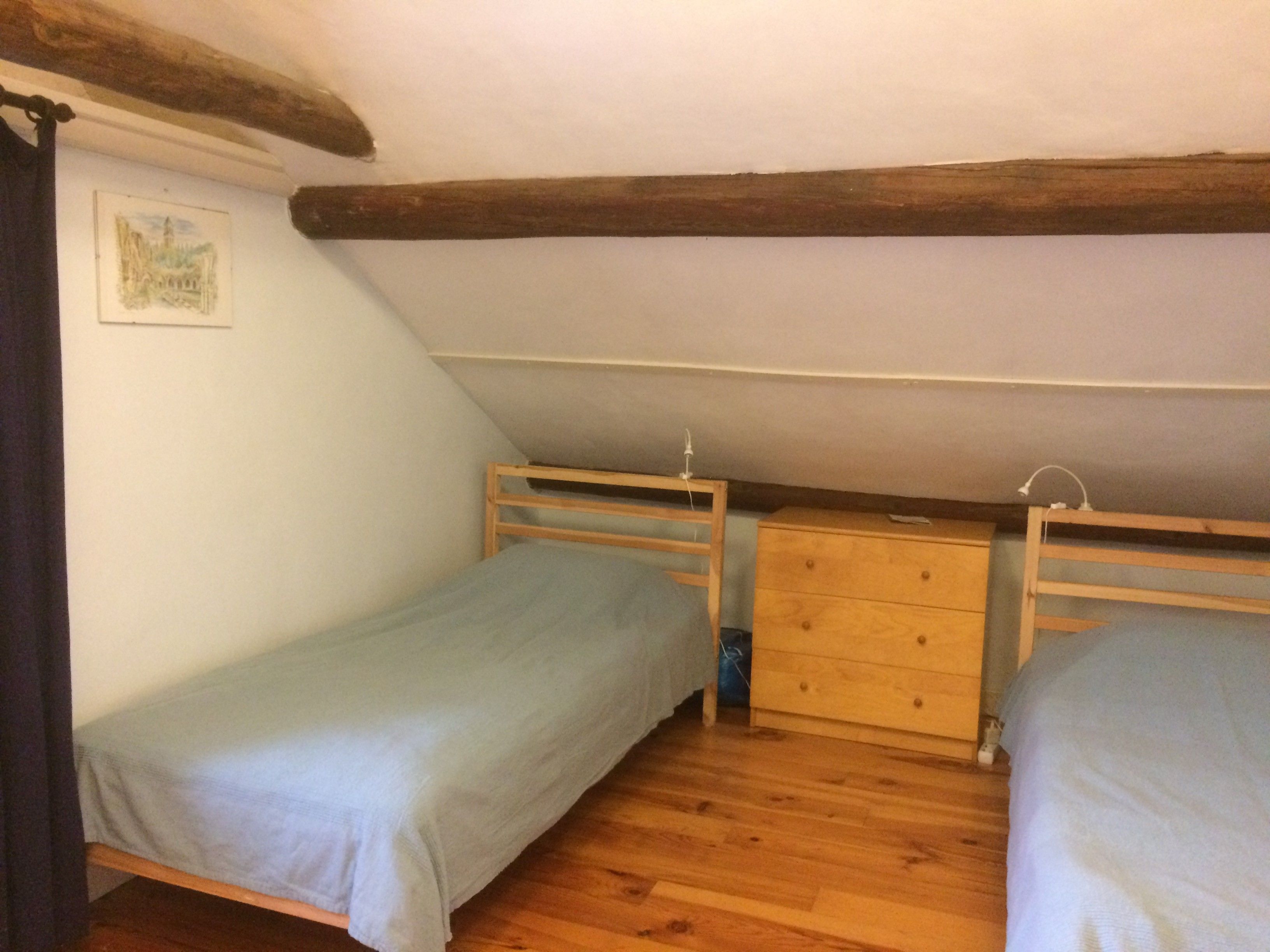 A small, simple room with two single beds, a wooden dresser, and a sloped ceiling.