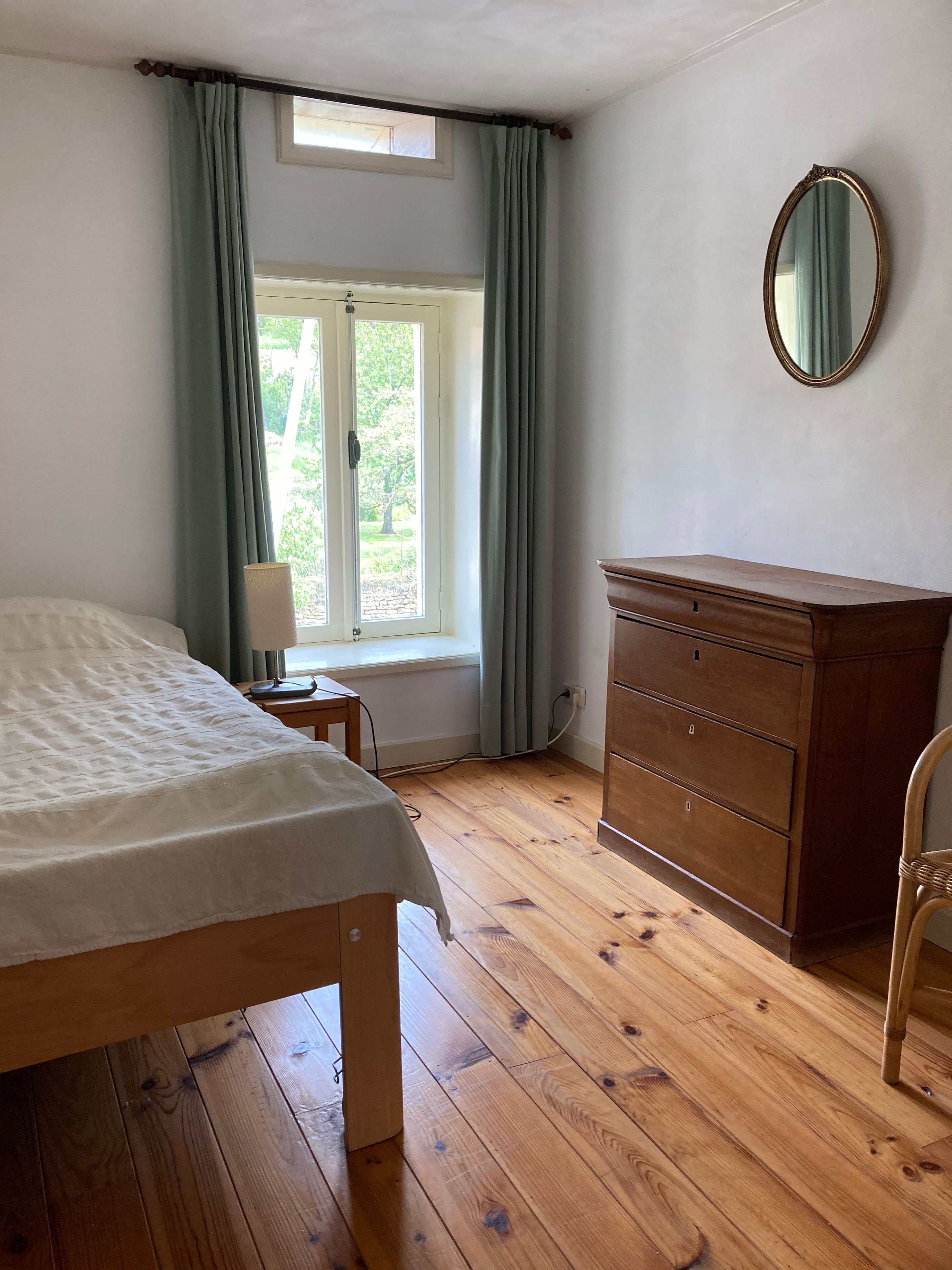 Ein Schlafzimmer mit einem hölzernen Bett, einem Schminktisch, einem Spiegel und einem Fenster mit Vorhängen.