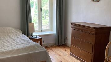 Ein Schlafzimmer mit einem hölzernen Bett, einem Schminktisch, einem Spiegel und einem Fenster mit Vorhängen.