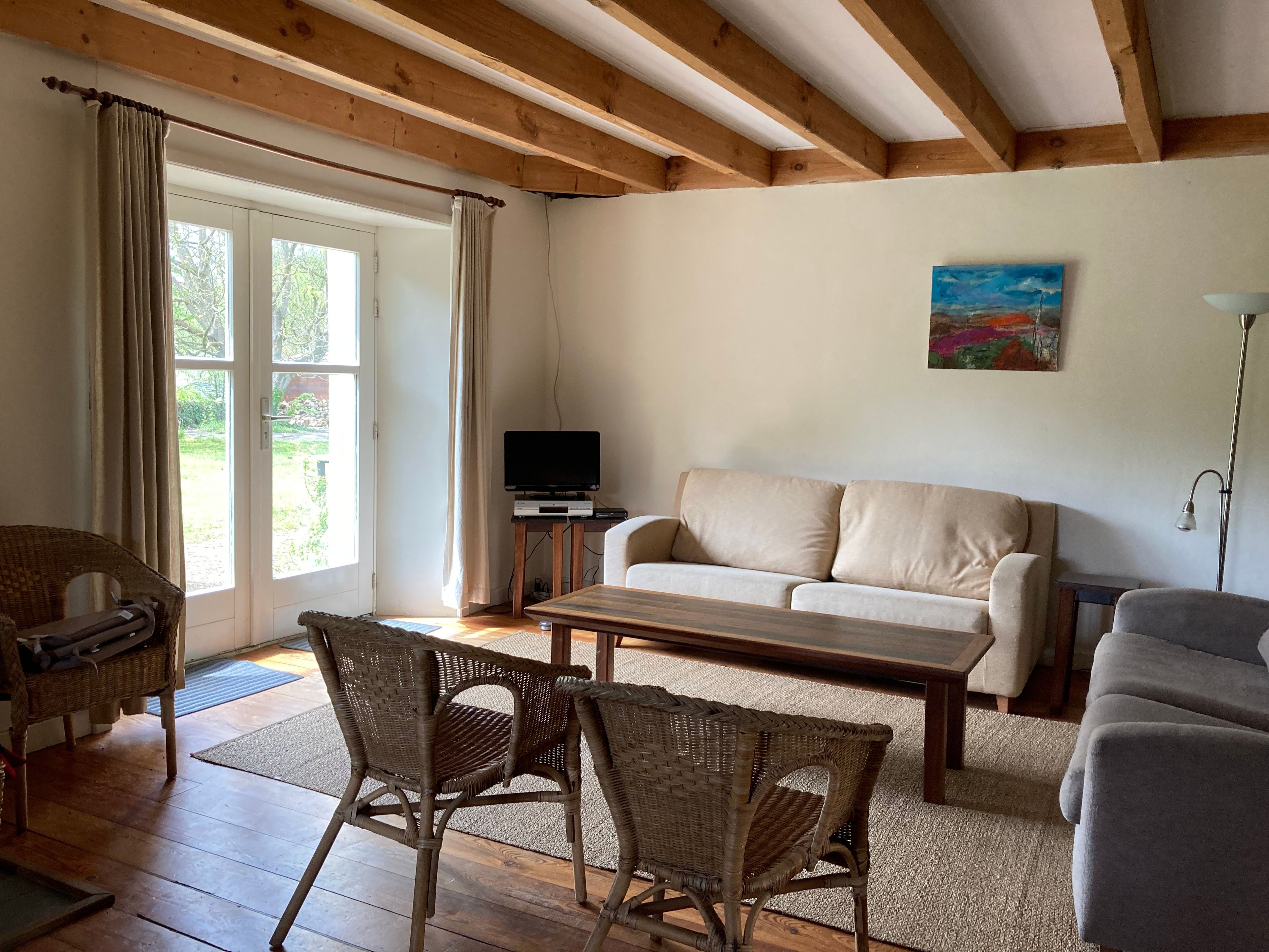 A living room with a sofa, two wicker chairs, a coffee table, a television on a stand, and a painting on the wall.