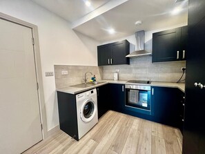A compact kitchen with a washing machine, oven, and modern cabinetry. - Apartment Sleeps 5 Near High Street (Croydon)