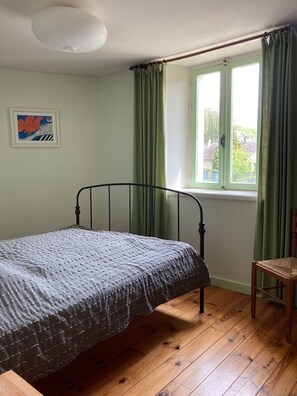 Una habitación con una cama individual, una silla, una ventana con cortinas y una lámpara en el techo.