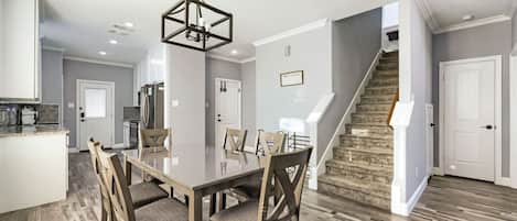 Un comedor amplio con una mesa grande y sillas, una cocina al fondo y una escalera que sube a otro nivel.