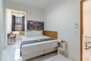 A hotel room with a bed, a desk, a chair, a small table, a painting on the wall, and a window with curtains. - Spacious 1BR Near Metro Copacabana Br1102 (Rio de Janeiro)
