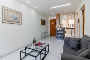 A modern living room with a glass coffee table, a grey sofa, and a bookshelf. - Spacious 1BR Near Metro Copacabana Br1102 (Rio de Janeiro)