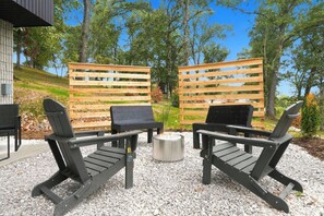 Ein Sitzbereich im Freien mit zwei schwarzen Adirondack-Stühlen und einem kleinen runden Tisch, umgeben von einem Holzzaun und einem Kiesgrund.