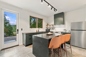 A modern kitchen with a central island, stainless steel appliances, and a view of the outdoors. - The Cardinal | Wooded Cabin Stay Near Downtown + Trails (Bentonville)