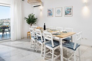A dining area with a table set for four, white chairs with blue cushions, a potted plant, and framed artwork on the wall. - Casa Alborán | Jacuzzi | Billiard | BBQ | Sea view (Málaga)