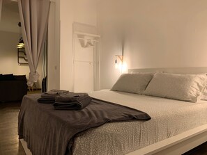 Un lit bien fait, avec une couvre-lit à motifs, une serviette pliée et un luminaire fixé au mur.