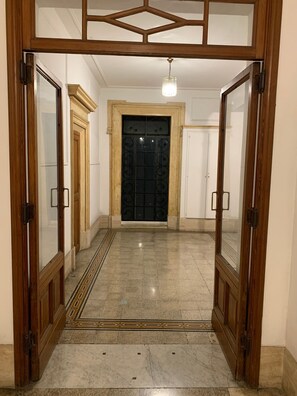 Ein Korridor mit Fliesenboden, einer zentralen Tür mit Zierdekor und je einer Holztür mit Glasfenstern zur Seite.