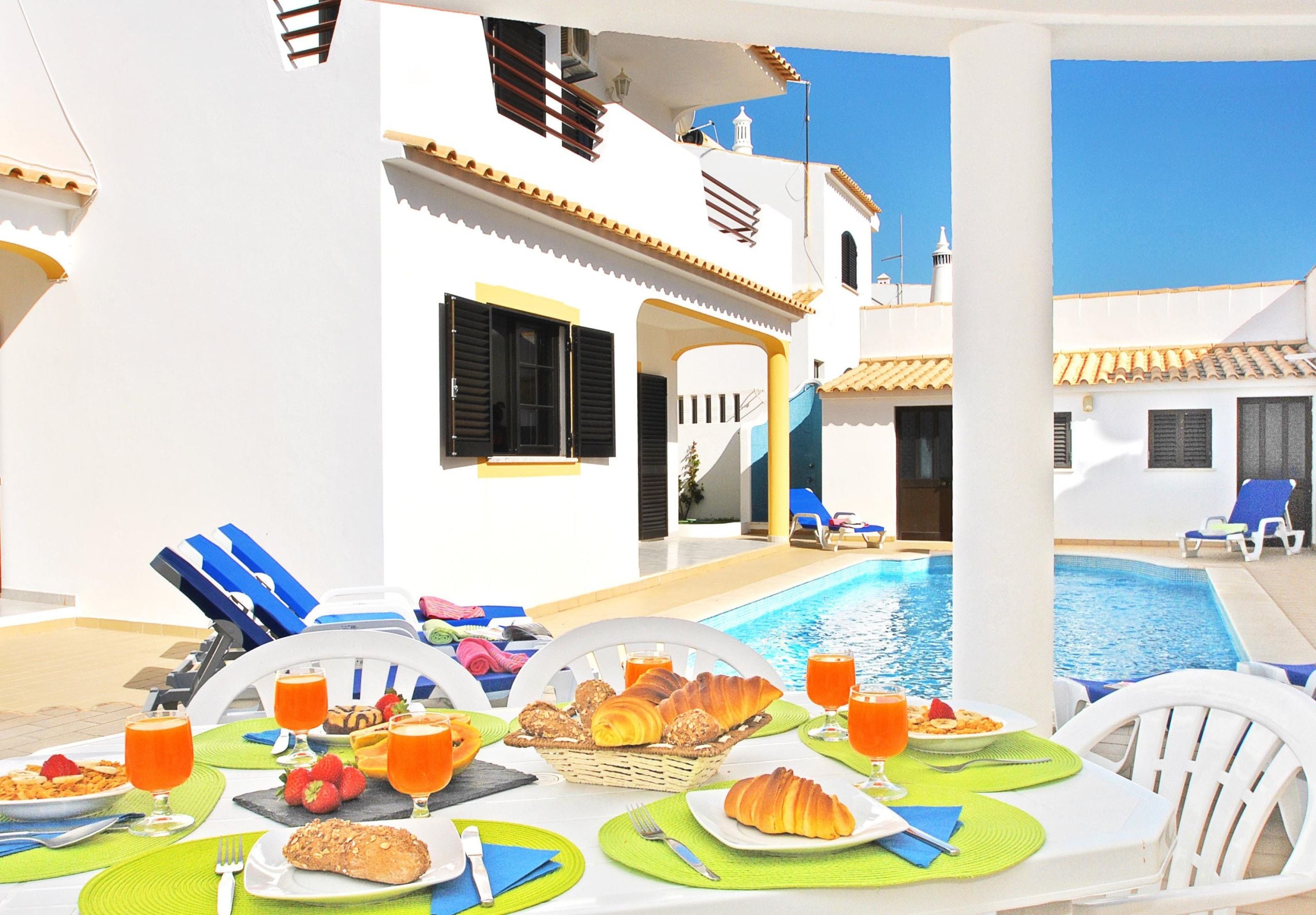 A poolside dining area with tables set for breakfast, overlooking a swimming pool.