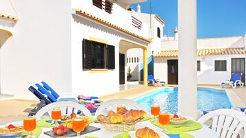 Un espace repas aménagé au bord de la piscine, avec des tables préparées pour le petit-déjeuner, donnant sur une piscine.