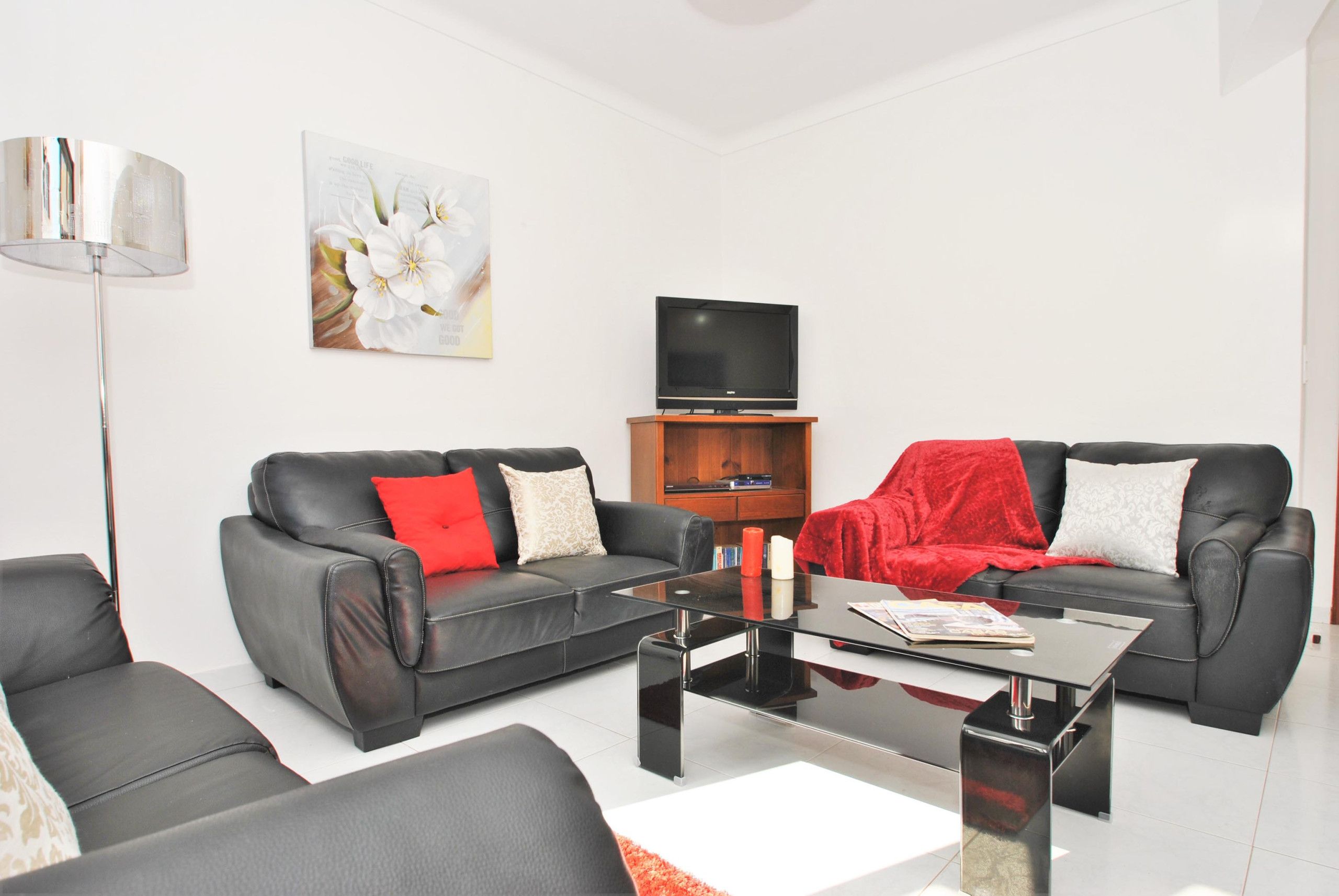 A modern living room with two black leather sofas, a glass coffee table, a flat-screen TV, and a floor lamp.