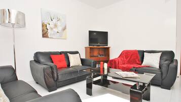 A modern living room with two black leather sofas, a glass coffee table, a flat-screen TV, and a floor lamp.