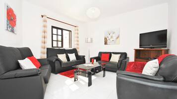 A living room with two black sofas, a glass coffee table, a TV, and a window with curtains.