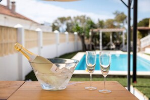 Une scène au bord de la piscine, avec une bouteille de champagne dans un seau, deux verres et une piscine en arrière-plan.