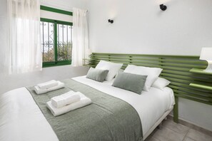 Un lit bien fait, avec du linge de lit blanc et un plaid vert, une fenêtre avec des rideaux blancs et une tête de lit verte.