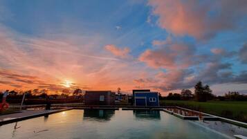 A calm body of water reflecting the sky, surrounded by small buildings and a grassy field.