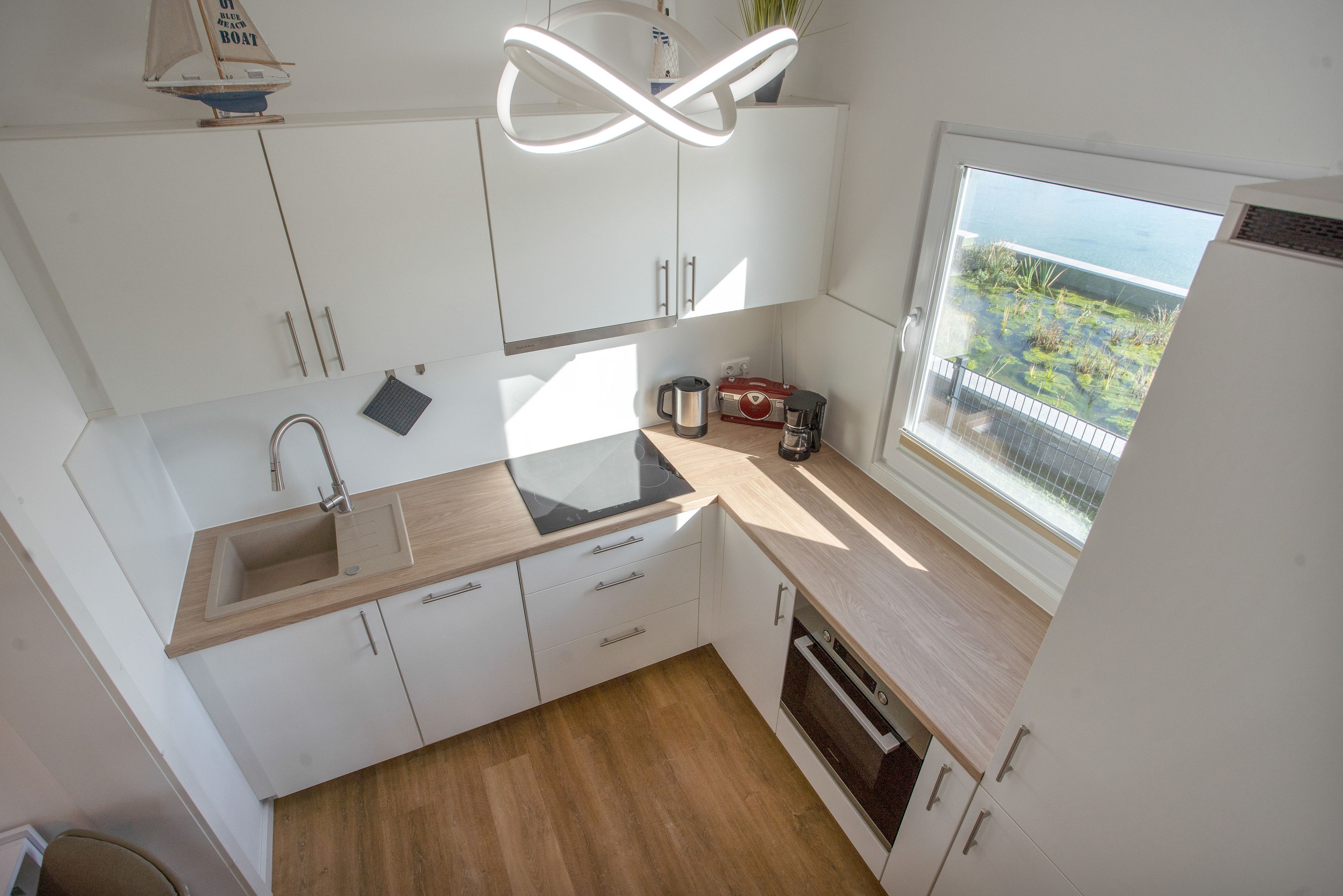 Eine moderne Küche mit Holzarbeitsplatte, weißen Schränken, einem eingebauten Ofen und Blick auf einen Balkon mit Grünpflanzen.
