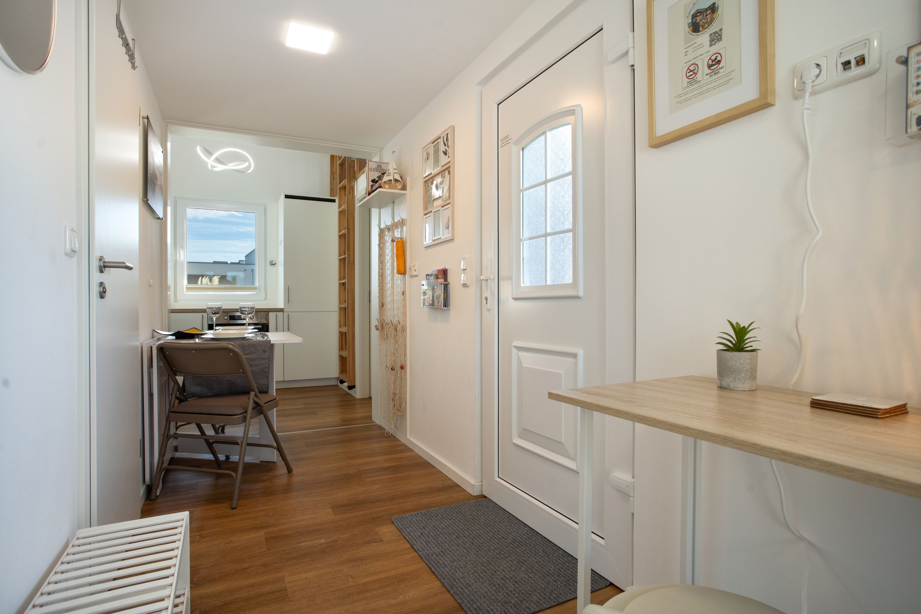 A narrow hallway with a kitchen area, a dining table, and a small seating area.