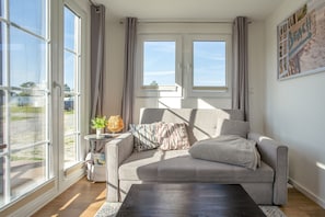 A modern living room with a sofa, a coffee table, and a view of the outdoors through large windows.