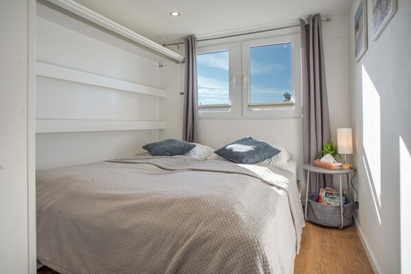 A bedroom with a bed, pillows, a bedside table with a lamp, a window, and a view of the sky.