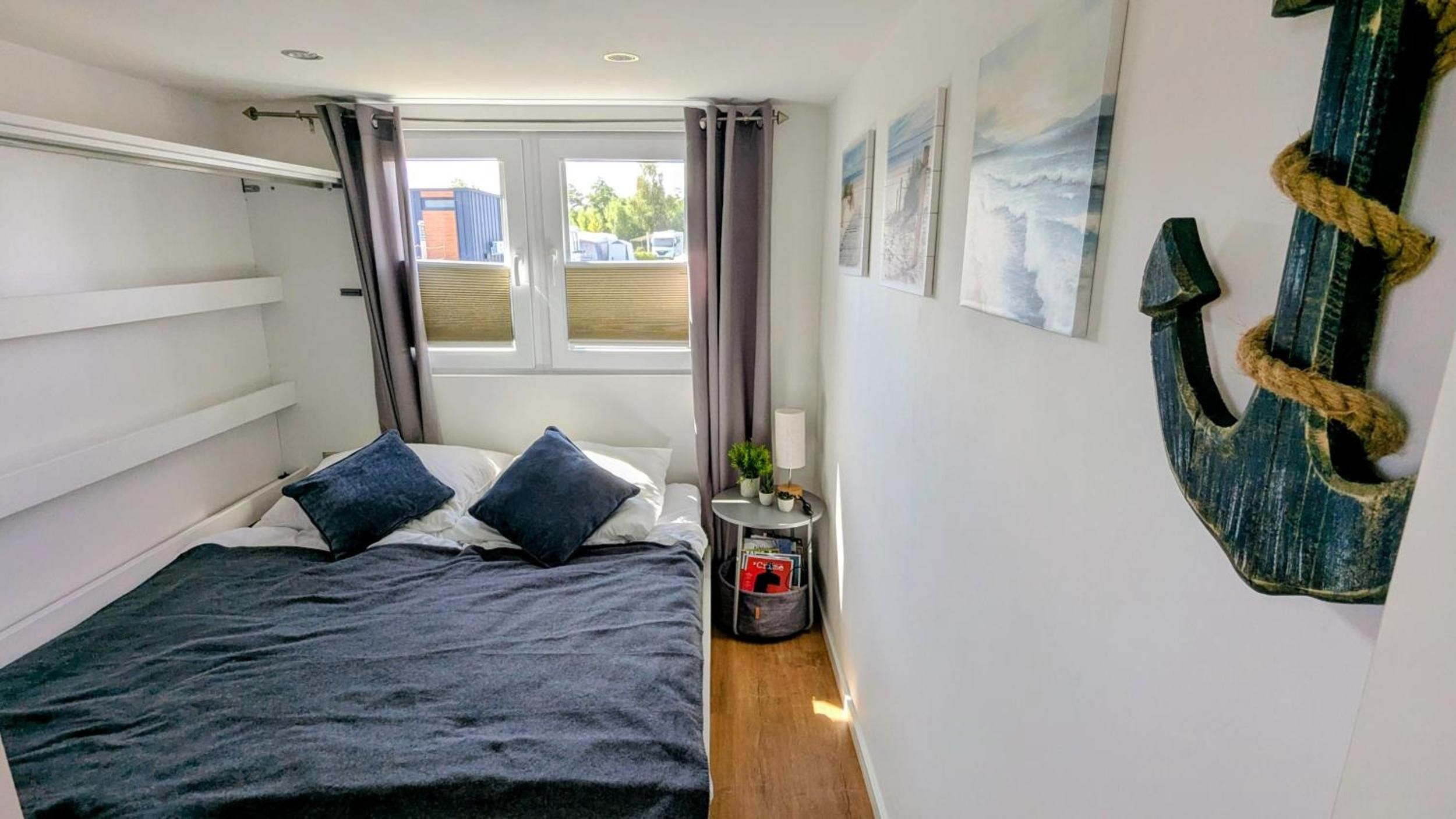 A bedroom with a bed, curtains, a small table with a lamp, and a wall-mounted decoration.