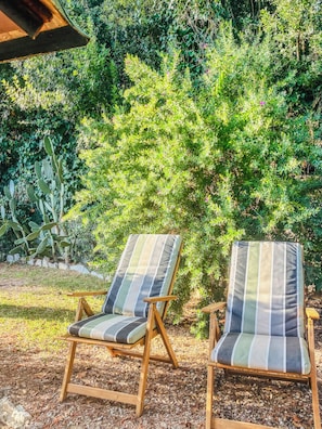Two striped lounge chairs with wooden frames and cushions, positioned on a gravel surface with a backdrop of dense green foliage and a cactus plant. - Casa Nora (Rosignano Solvay-Castiglioncello)