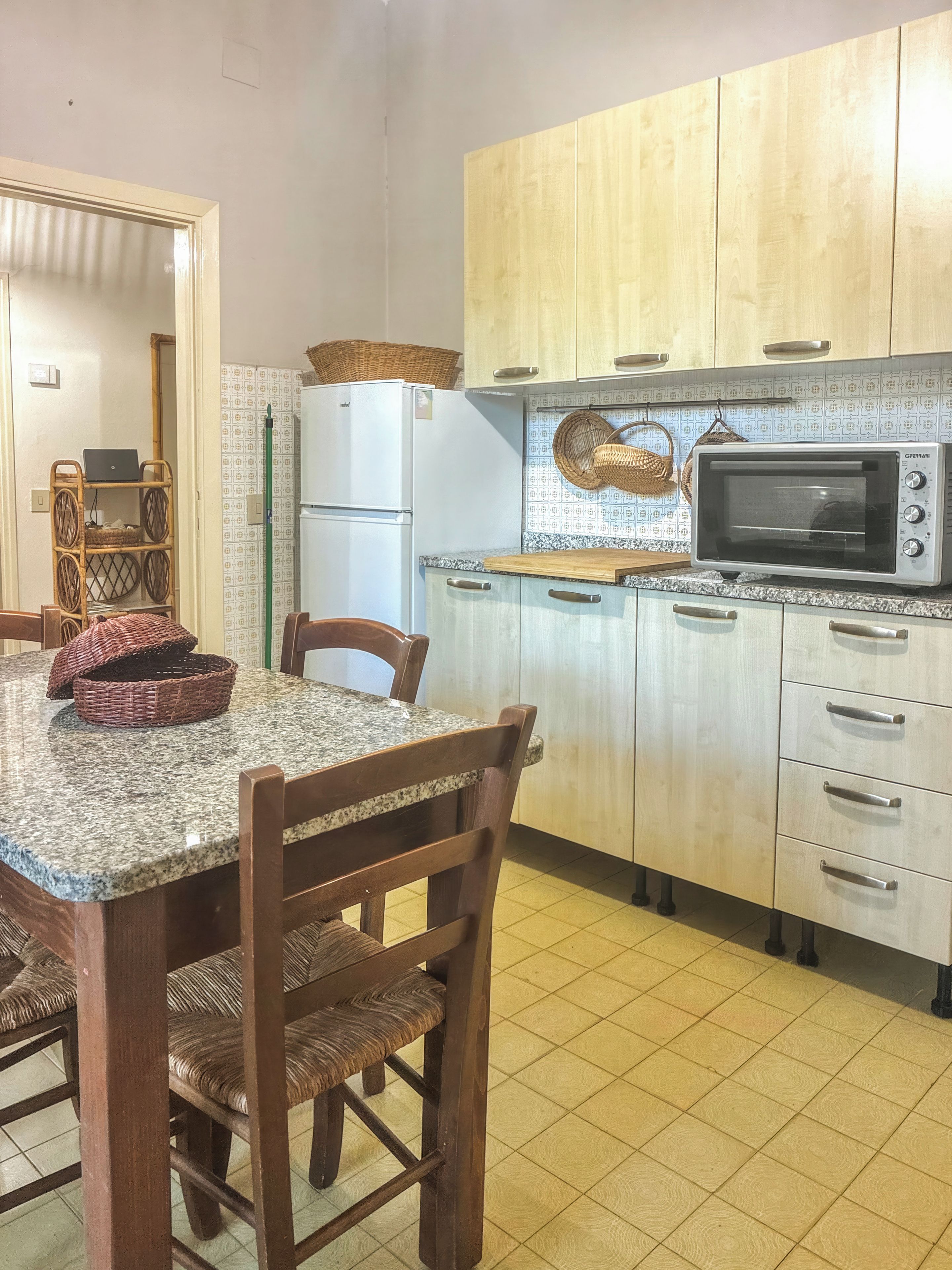 A kitchen with a granite countertop, wooden chairs, a microwave, and a refrigerator.