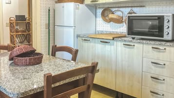 A kitchen with a granite countertop, wooden chairs, a microwave, and a refrigerator.