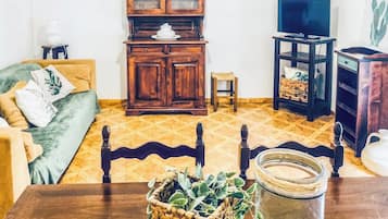 A living room with a sofa, wooden cabinet, television, and a dining table with a vase.