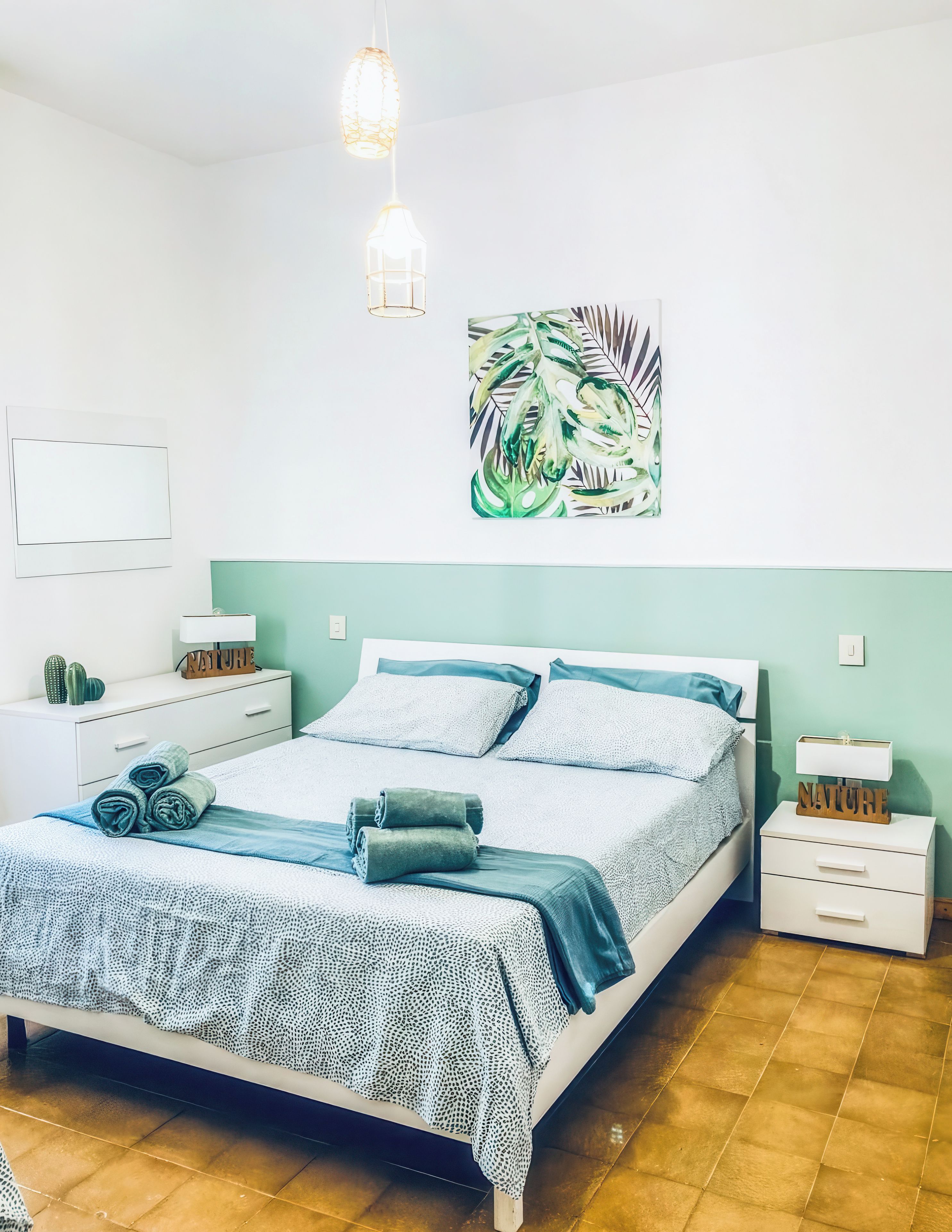 Une chambre à coucher comprenant un lit, des tables de chevet, une œuvre d’art murale et un luminaire suspendu.
