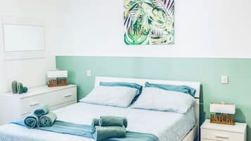 Une chambre à coucher comprenant un lit, des tables de chevet, une œuvre d’art murale et un luminaire suspendu.