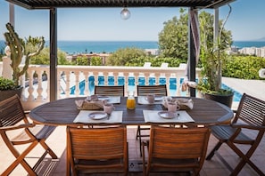 An outdoor dining area with a view of the sea, wooden furniture, and a pool in the background. - Villa Botanic | Pool | Ping Pong | Fireplace (Rincon de la victoria)