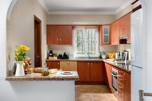 A kitchen with wooden cabinets, a granite countertop, a built-in oven, and a window with a view of greenery. - Villa Selvatic | Pool | Cinema | Sauna | Mini Golf (Arenas)