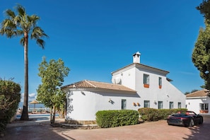 A white building with a tiled roof, surrounded by greenery and a parked car. - Villa Selvatic | Pool | Cinema | Sauna | Mini Golf (Arenas)