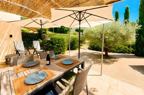 Een buiten eethoek met een houten tafel, stoelen en parasols.