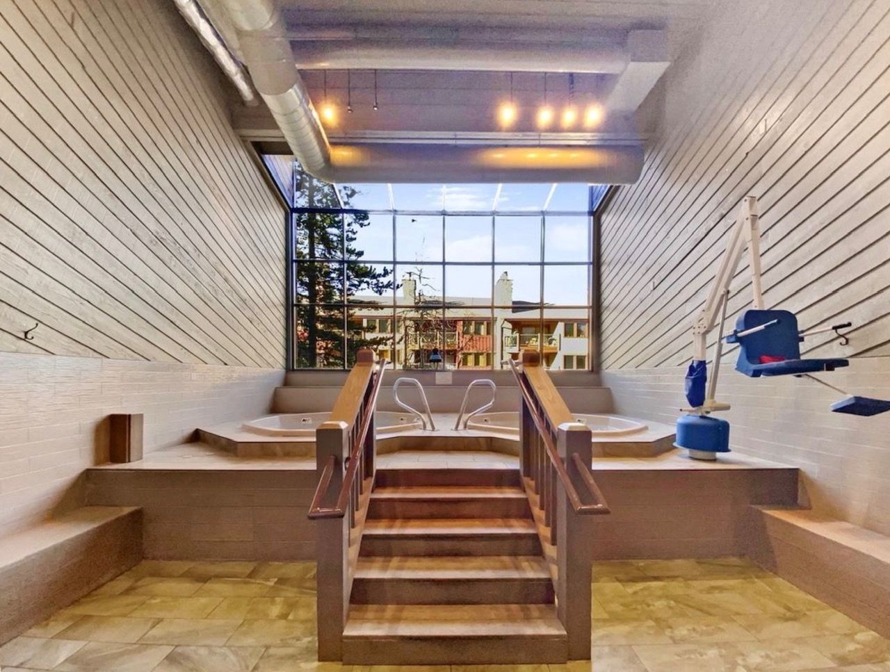 Een modern interieur met een centrale trap, uitzicht door grote ramen en een blauwe tandartsstoel.