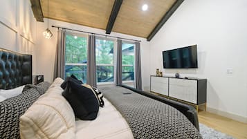 Une chambre à coucher avec un lit, une télévision, une commode et un balcon donnant sur la verdure.